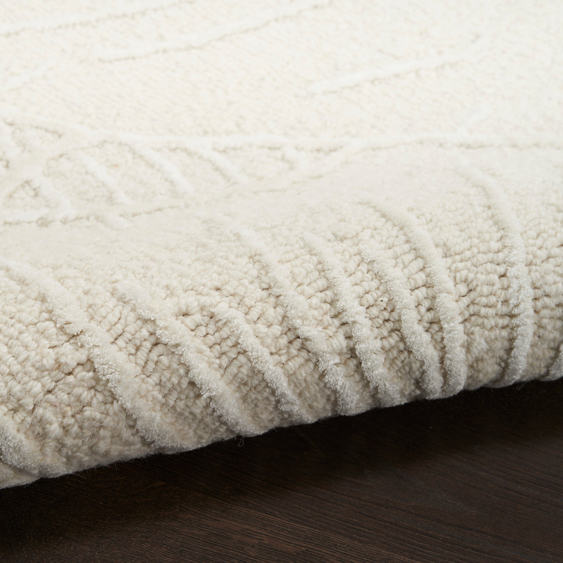 Cream ivory textured area rug with plush loop pile and ribbed edge on dark wood floor.