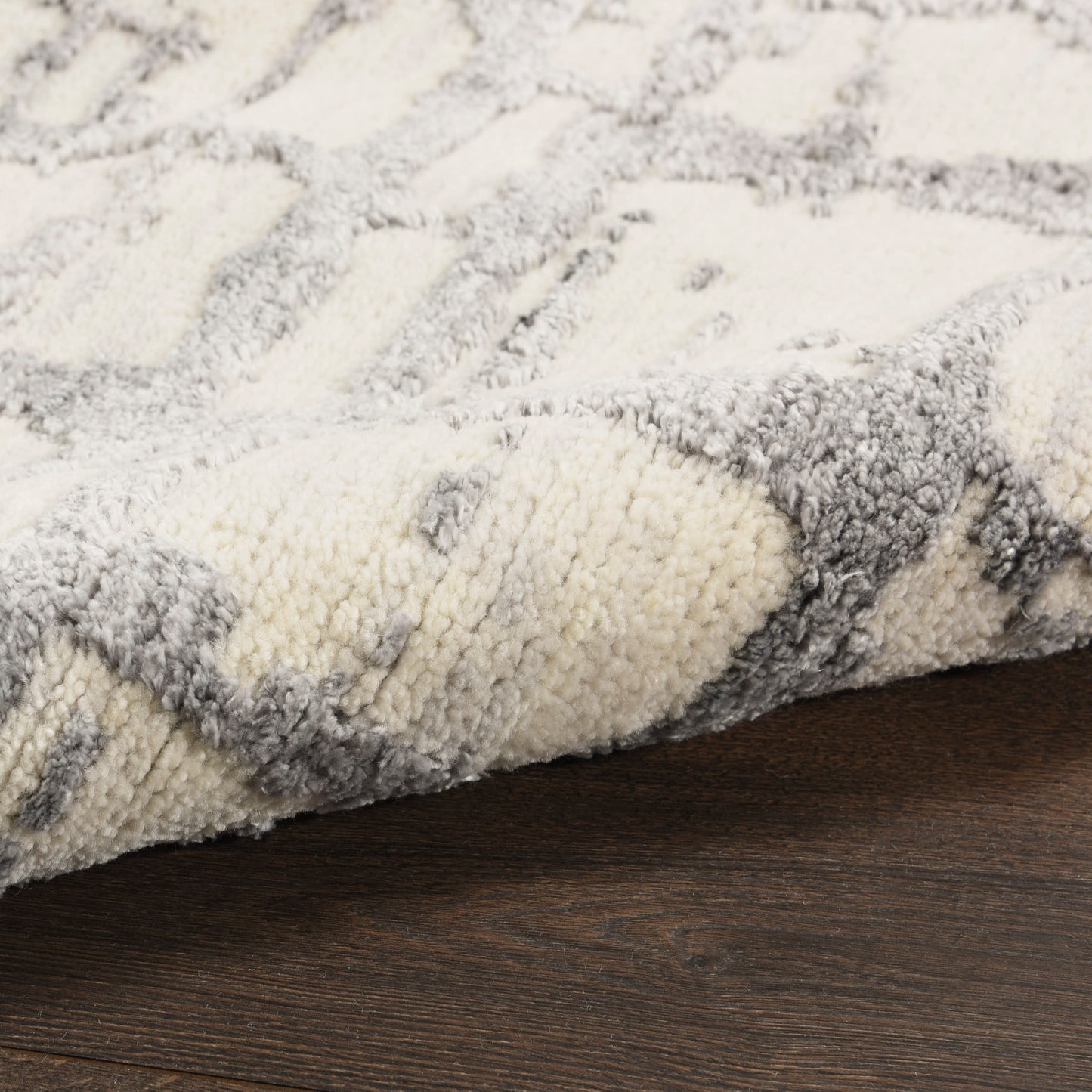 Close-up of a cream and gray shag rug with a geometric pattern on dark wood floor.