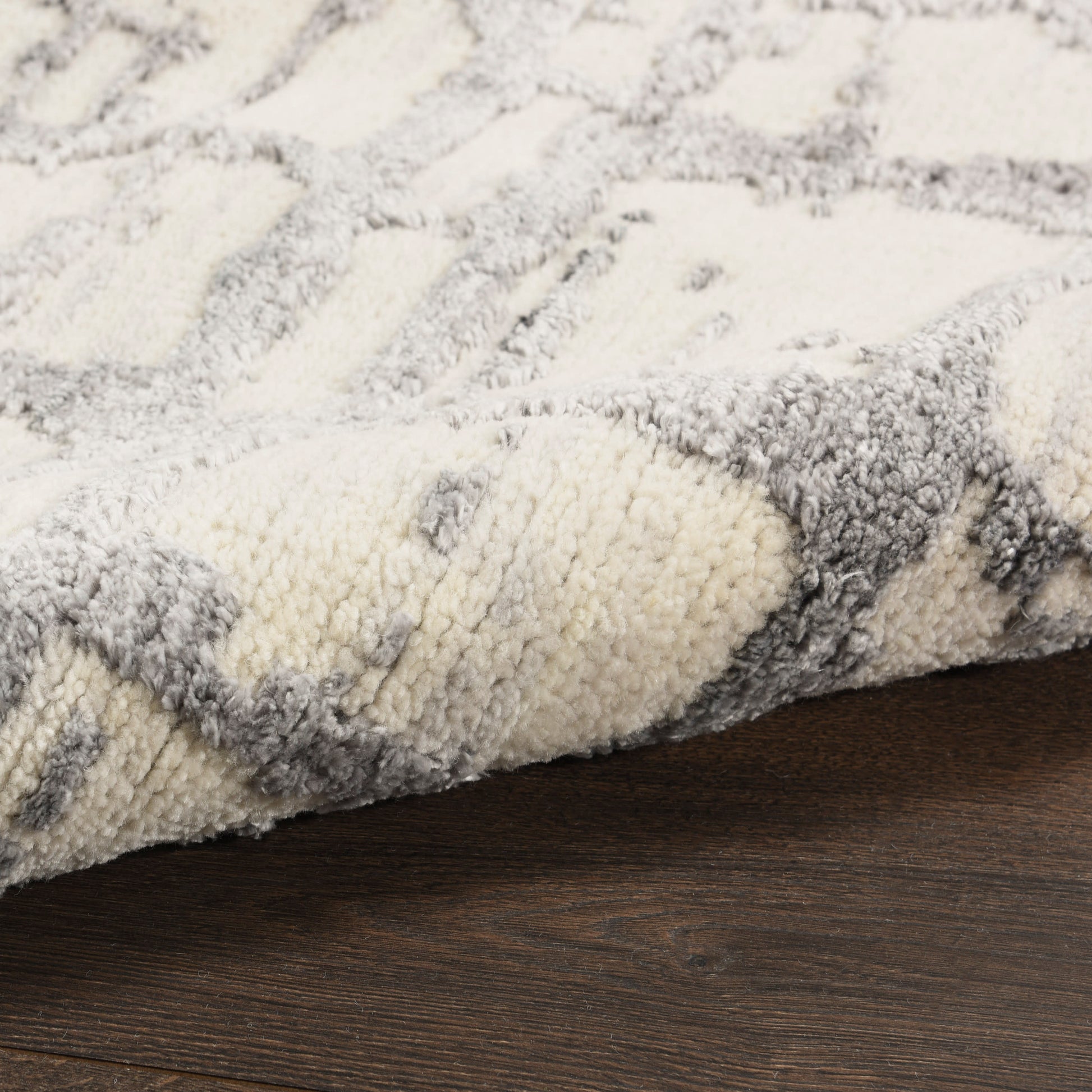 Close-up of a cream and gray shag rug with a geometric pattern on dark wood floor.