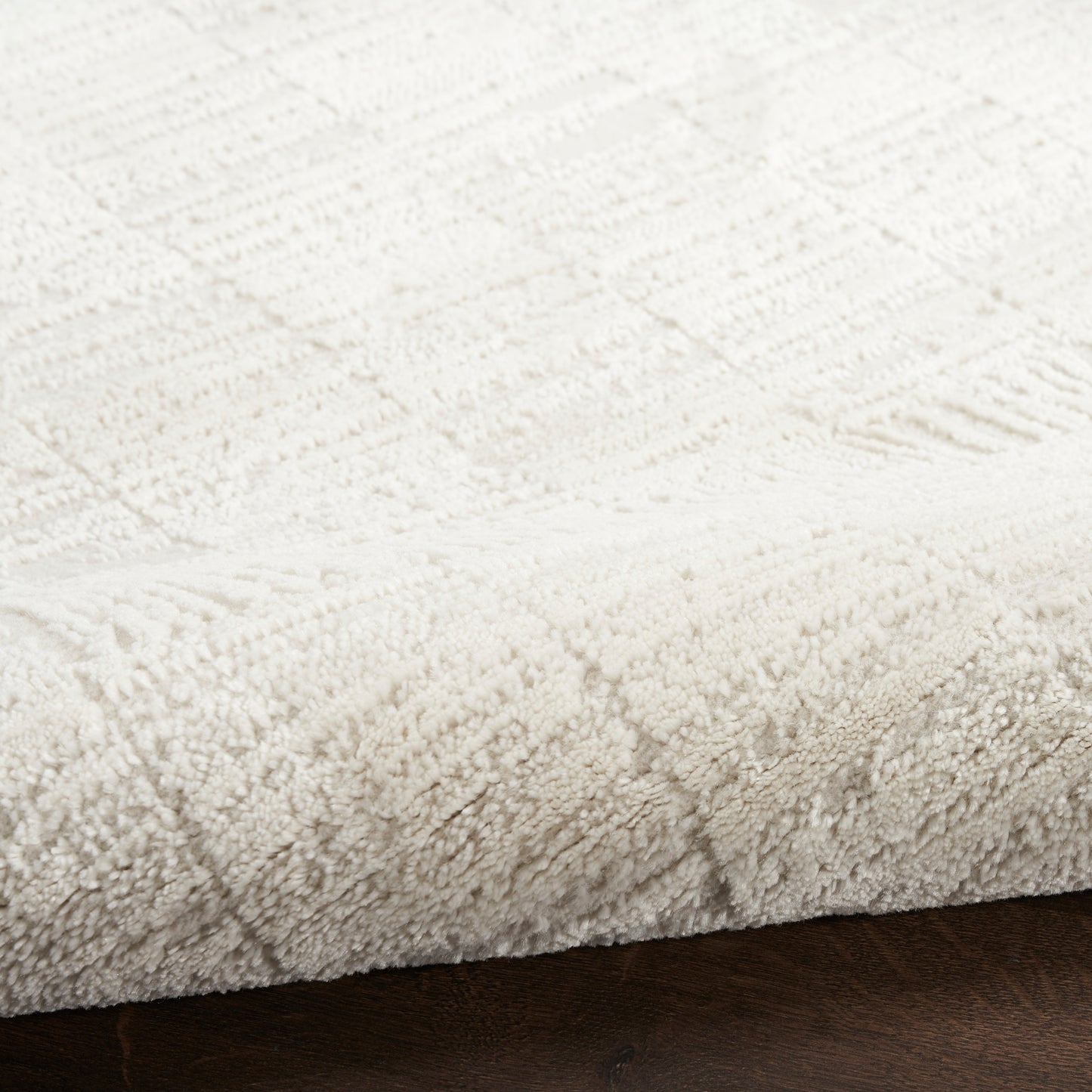 Cream plush rug with a raised geometric pattern on dark wood floor.