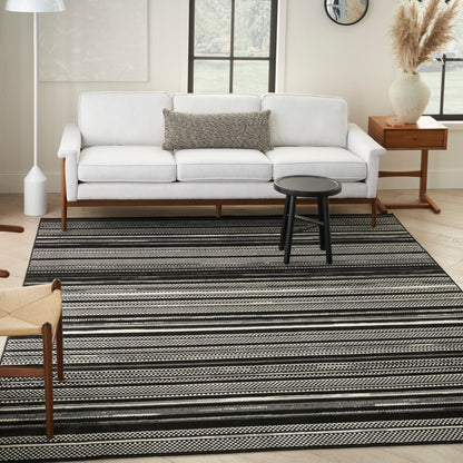 White sofa with wood legs, gray lumbar pillow, black round stool, and black-and-white striped rug in a bright living room.