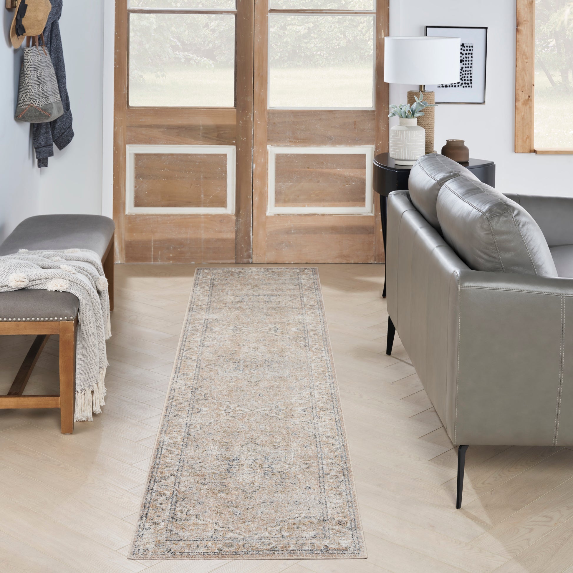 Neutral-toned distressed pattern runner rug along light wood floor, flanked by a gray leather sofa and wooden bench.