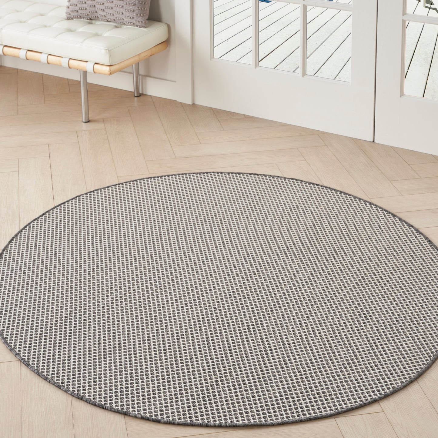 Round grey woven rug with small grid pattern on light wood floor by glass doors in bright living area