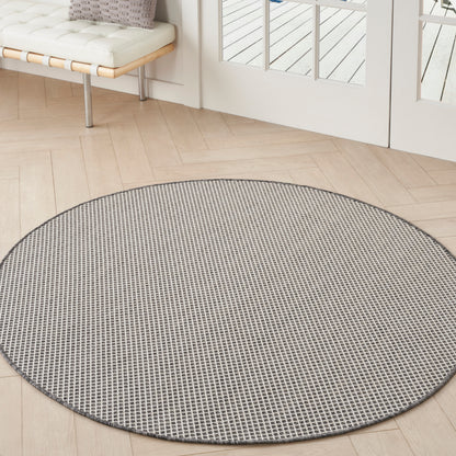 Round grey woven rug with small grid pattern on light wood floor by glass doors in bright living area