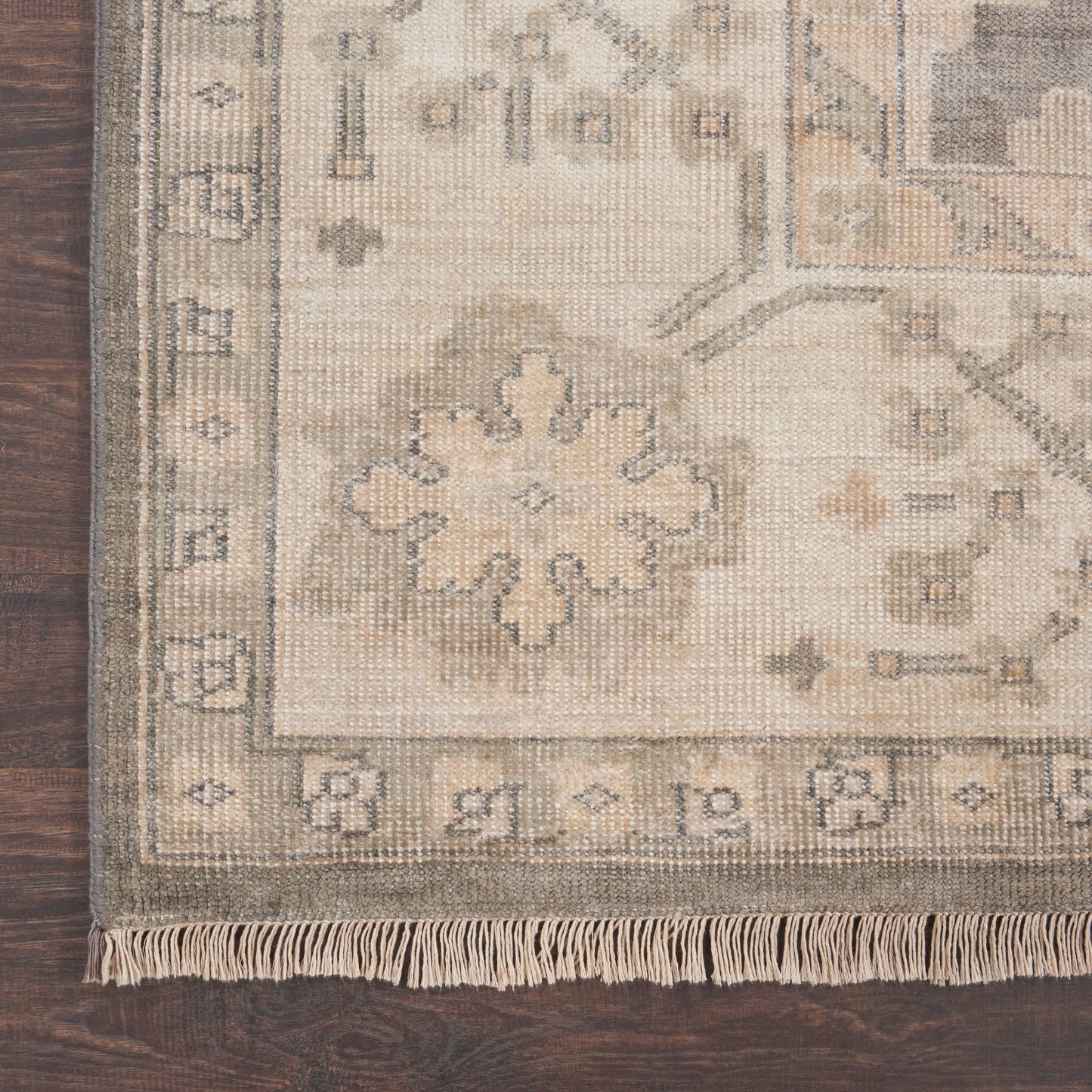 Beige cream oriental rug with floral medallion and border, fringed edge on dark wood floor.