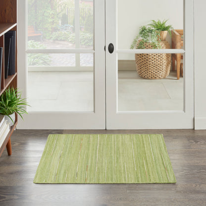 Green rectangular rug on dark wood floor in front of white-framed glass doors; cozy entryway with plants.