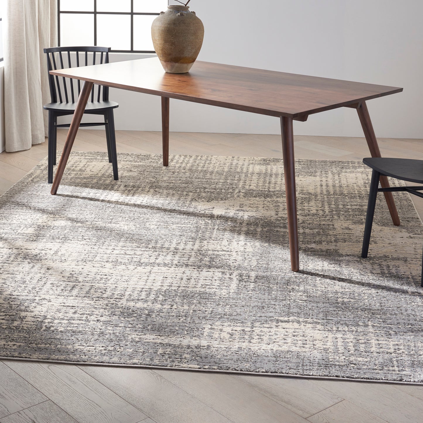 Rectangular walnut dining table with tapered legs, paired with black chairs and a ceramic vase centerpiece.