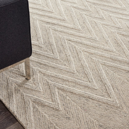 Beige herringbone carpet with a textured pattern; black upholstered chair leg visible on the left and dark wood floor edge.