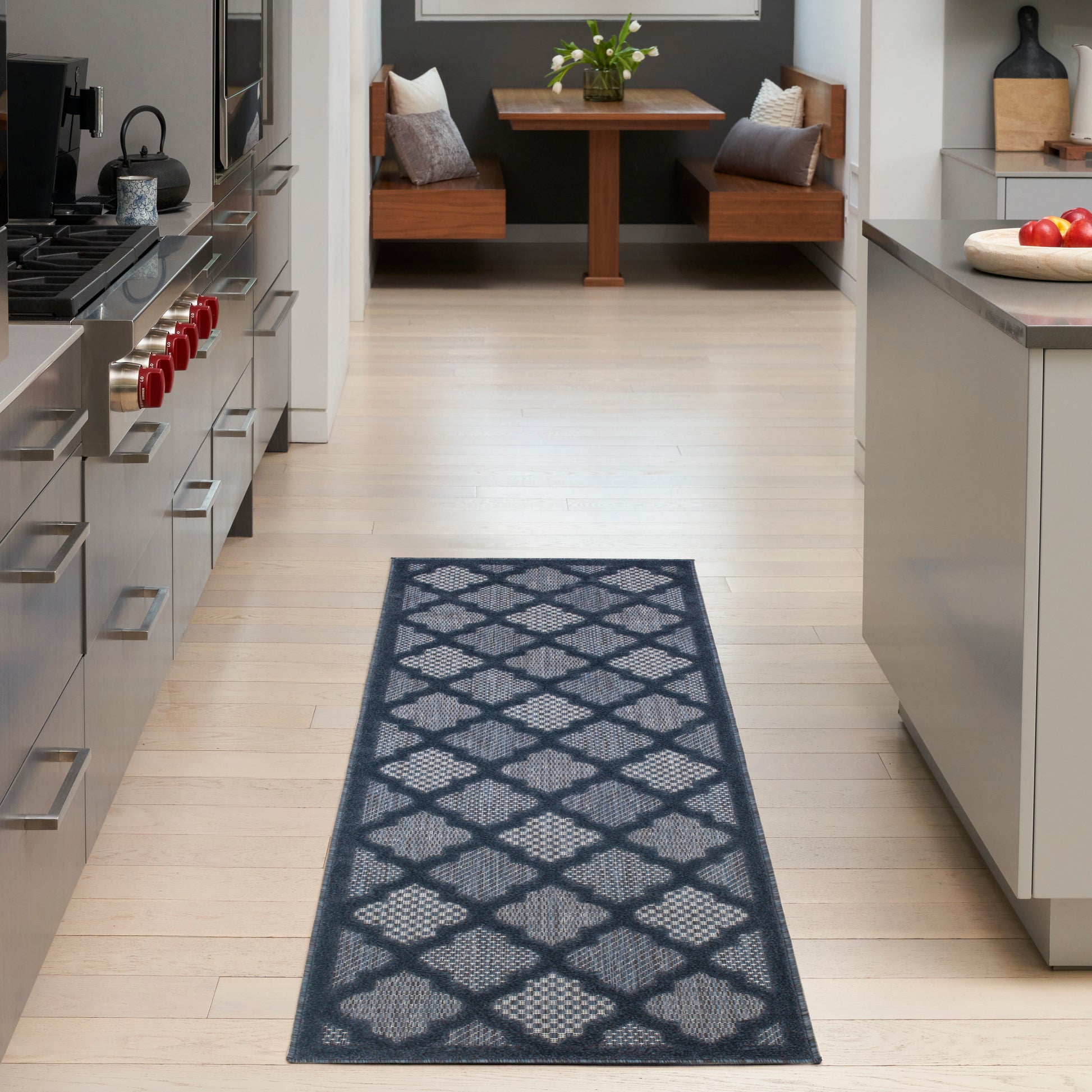 Blue-gray geometric lattice runner rug on light wood kitchen floor; modern stainless appliances and seating nook visible.