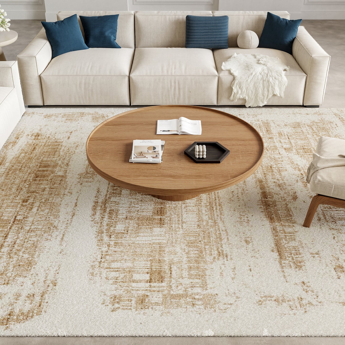 Cream patterned rug on the floor with a beige sectional sofa featuring blue cushions, a round wooden coffee table, and a white throw blanket nearby.