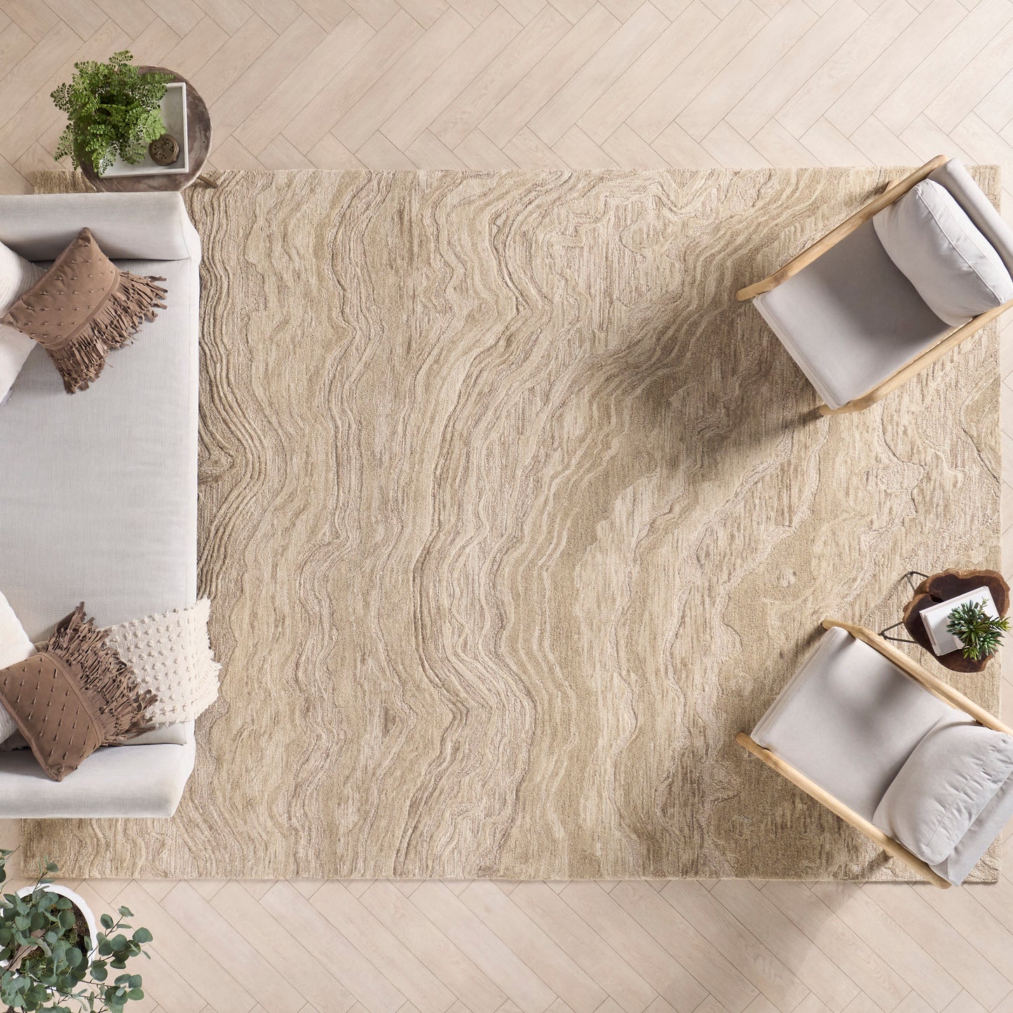 Beige textured area rug with wavy pattern under light wood floor, paired with cream sofa and two light wood chairs.