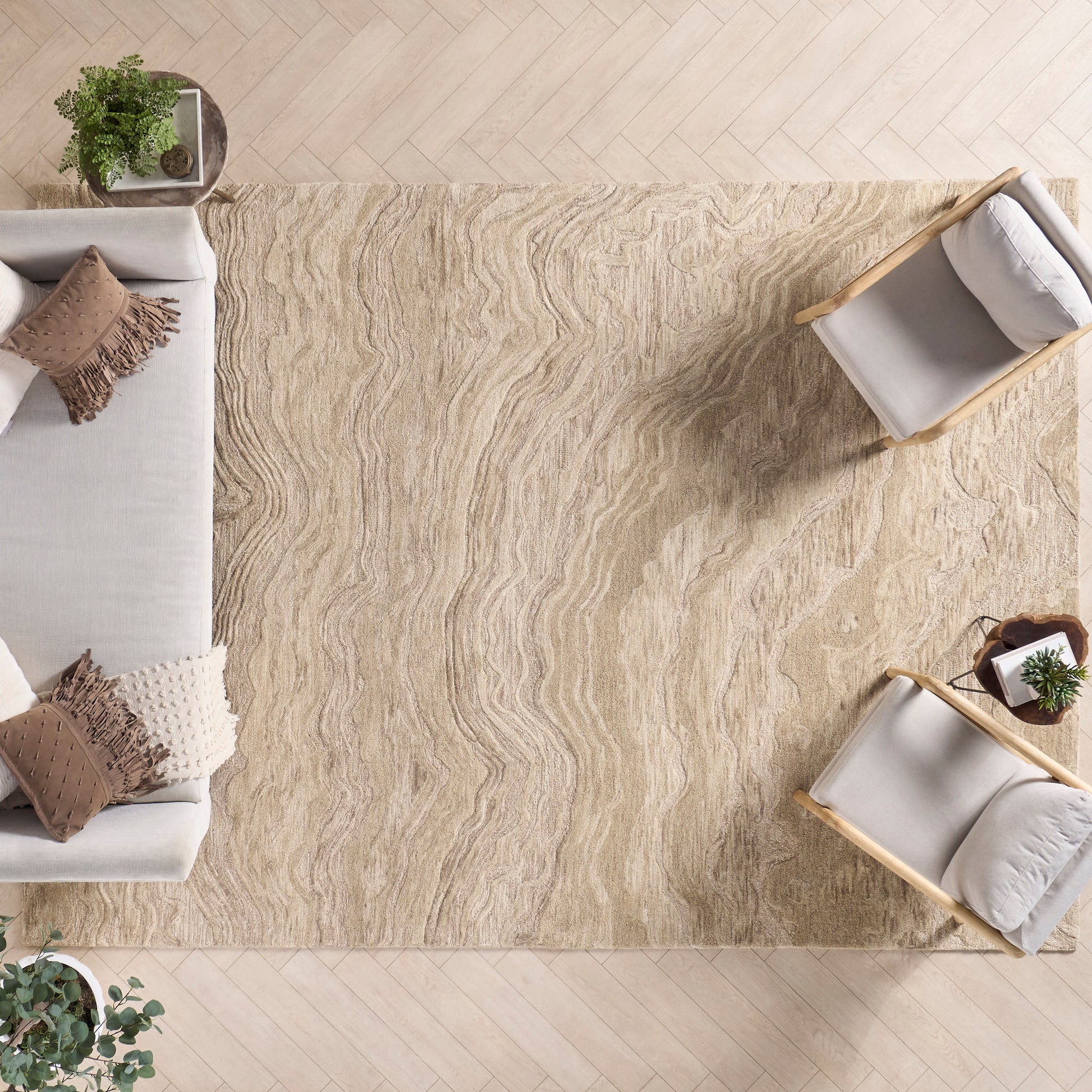 Beige textured area rug with wavy pattern under light wood floor, paired with cream sofa and two light wood chairs.