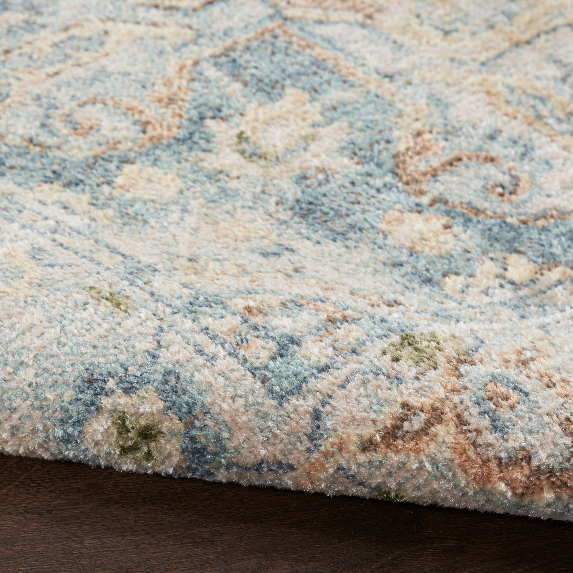 Close-up of a plush blue and ivory patterned area rug with sage green and tan accents on a dark wood floor.