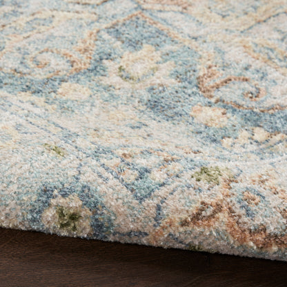 Close-up of a plush blue and ivory patterned area rug with sage green and tan accents on a dark wood floor.