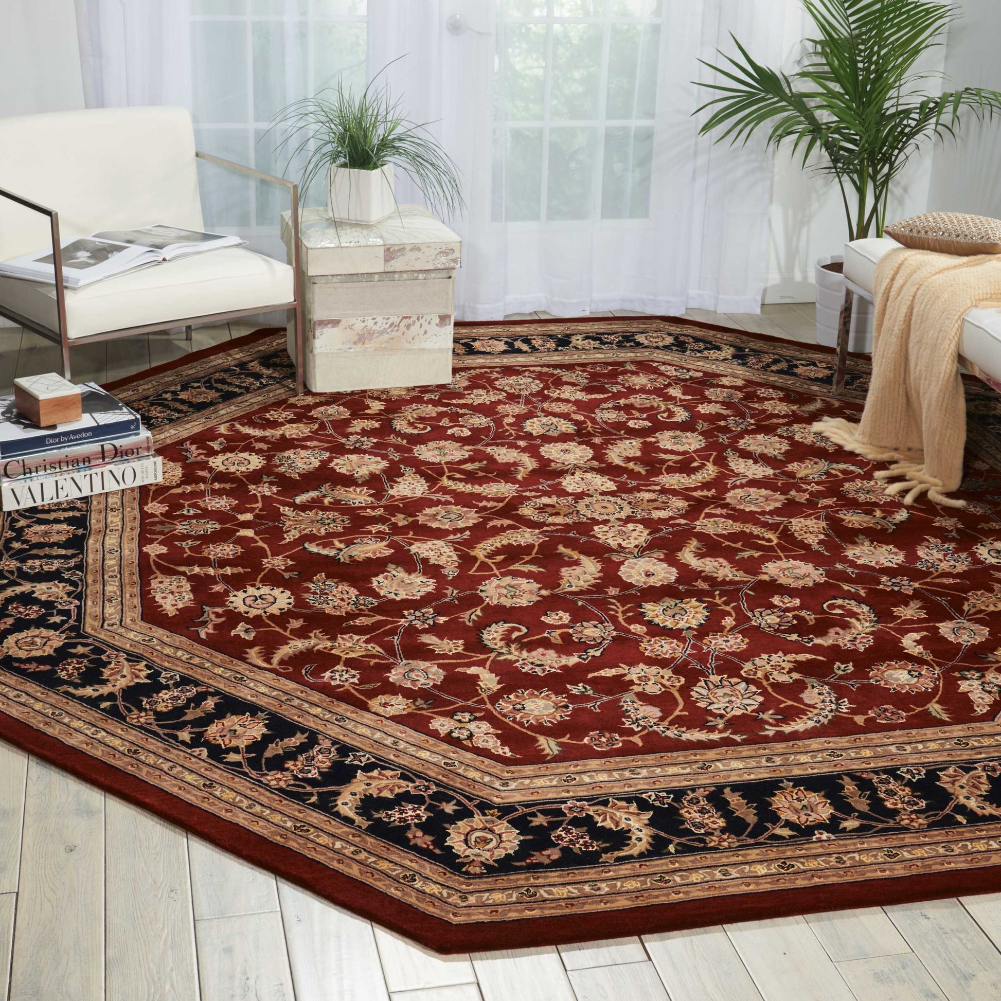 Large red Persian-style area rug with cream floral motifs and a dark navy border in a bright living room.