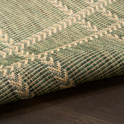 Teal-green woven rug with cream geometric pattern, folded edge on dark wood floor.