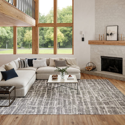 Bright modern living room with beige sectional, gray rug, white coffee table, wood-framed windows, and a stone fireplace.
