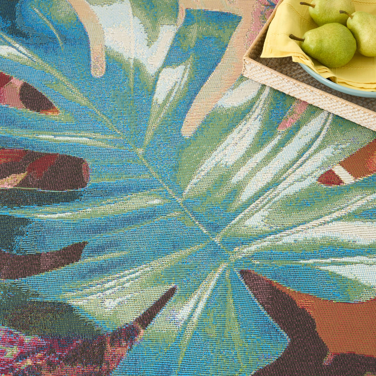 Rectangular tapestry rug with tropical blue-green leaf pattern; top-right wicker tray of pears on a yellow napkin.
