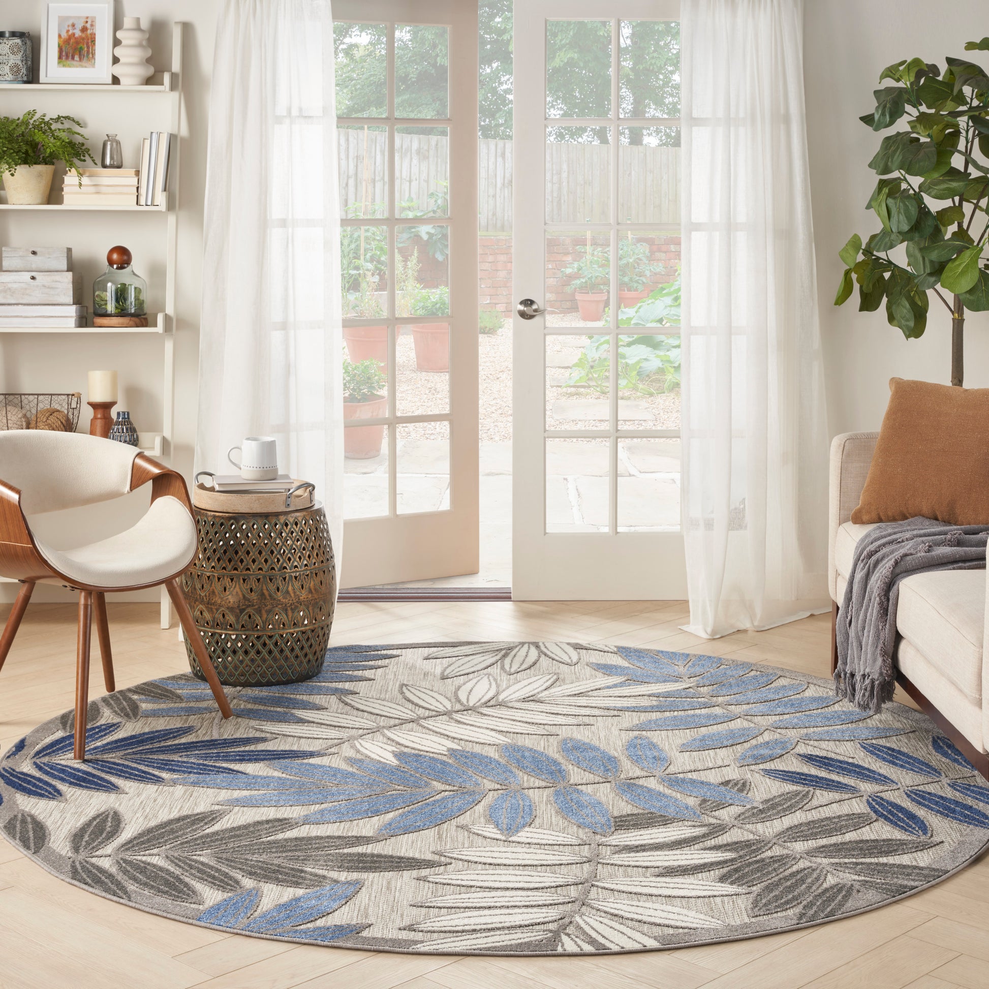 Round leaf-pattern rug in blue and gray tones on beige, in a bright living room with French doors and cream furniture.