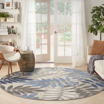 Round leaf-pattern rug in blue and gray tones on beige, in a bright living room with French doors and cream furniture.
