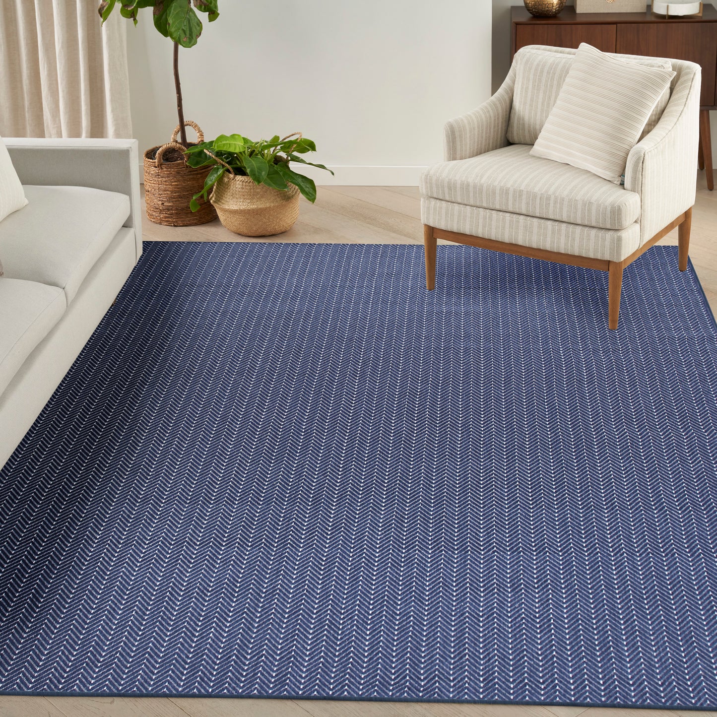 Blue chevron-pattern area rug in a living room with cream sofa, beige armchair, and potted plants in wicker baskets.