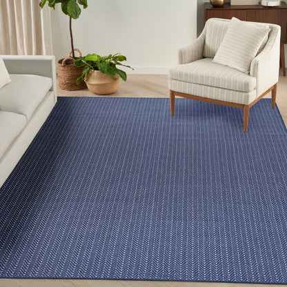 Blue chevron-pattern area rug in a living room with cream sofa, beige armchair, and potted plants in wicker baskets.