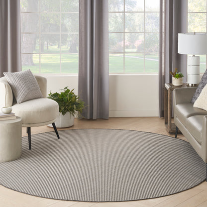 Round gray striped woven area rug in a bright living room with beige sofa, armchair, plants and gray curtains.