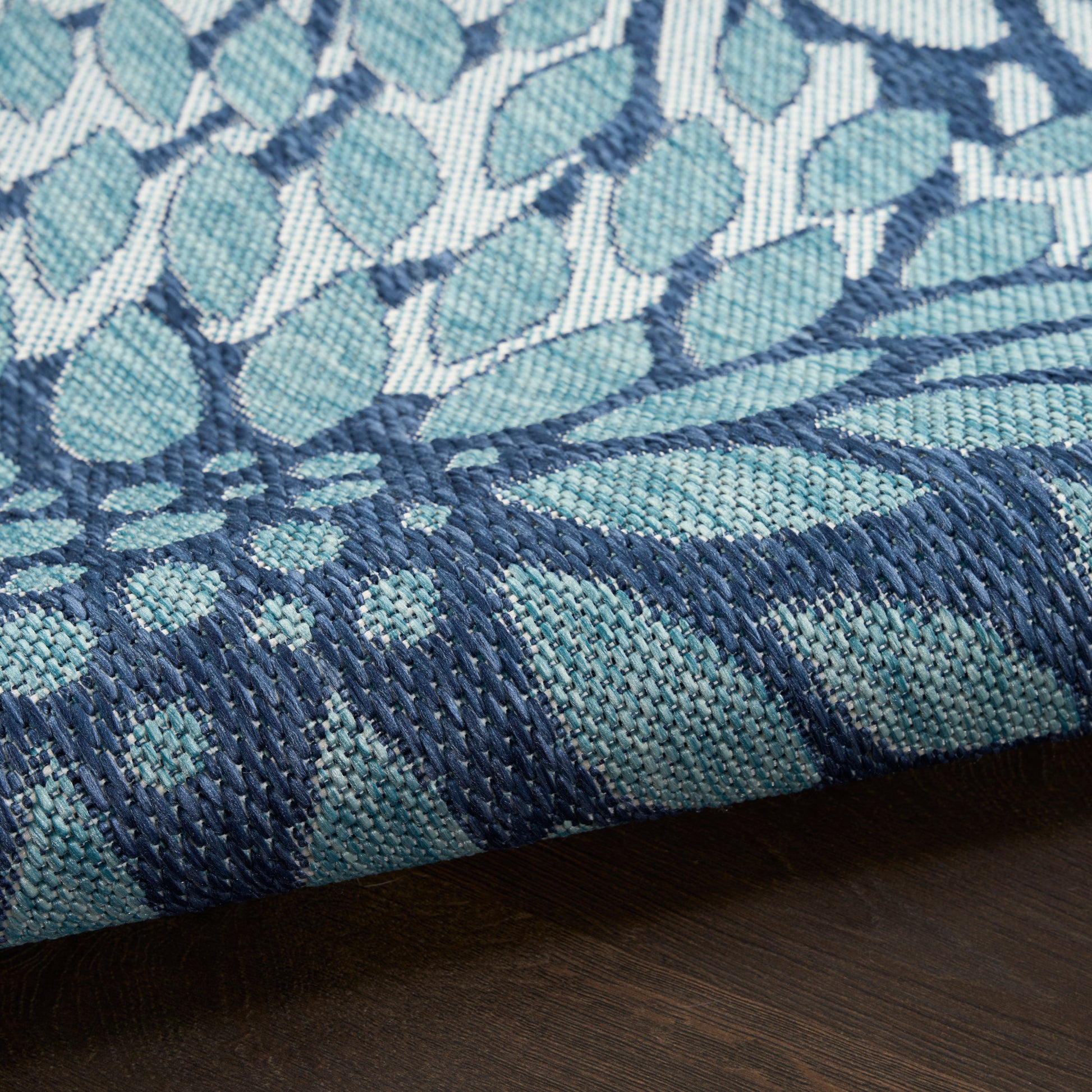 Close-up of teal and navy woven textile with leaf pattern; rolled edge on dark wood surface.