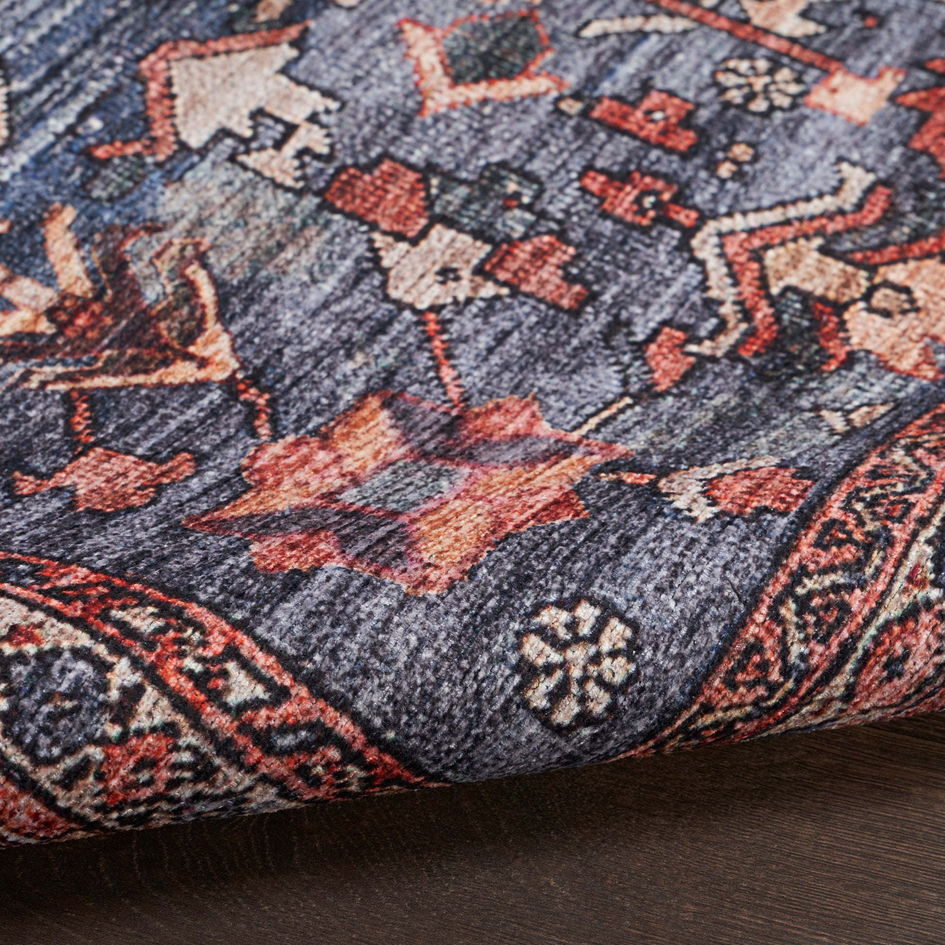 Close-up of blue Persian-style rug with red & cream floral motifs; woven wool look, folded corner on wood floor.