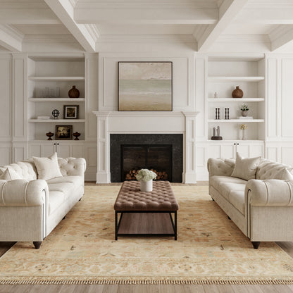 Neutral living room with cream tufted sofas facing a brown tufted ottoman, white built-in shelves, and a fireplace.