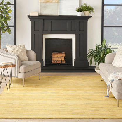 Black wooden mantel with paneled details, beige armchairs, a yellow rug, and leafy plants in a sunlit living room.