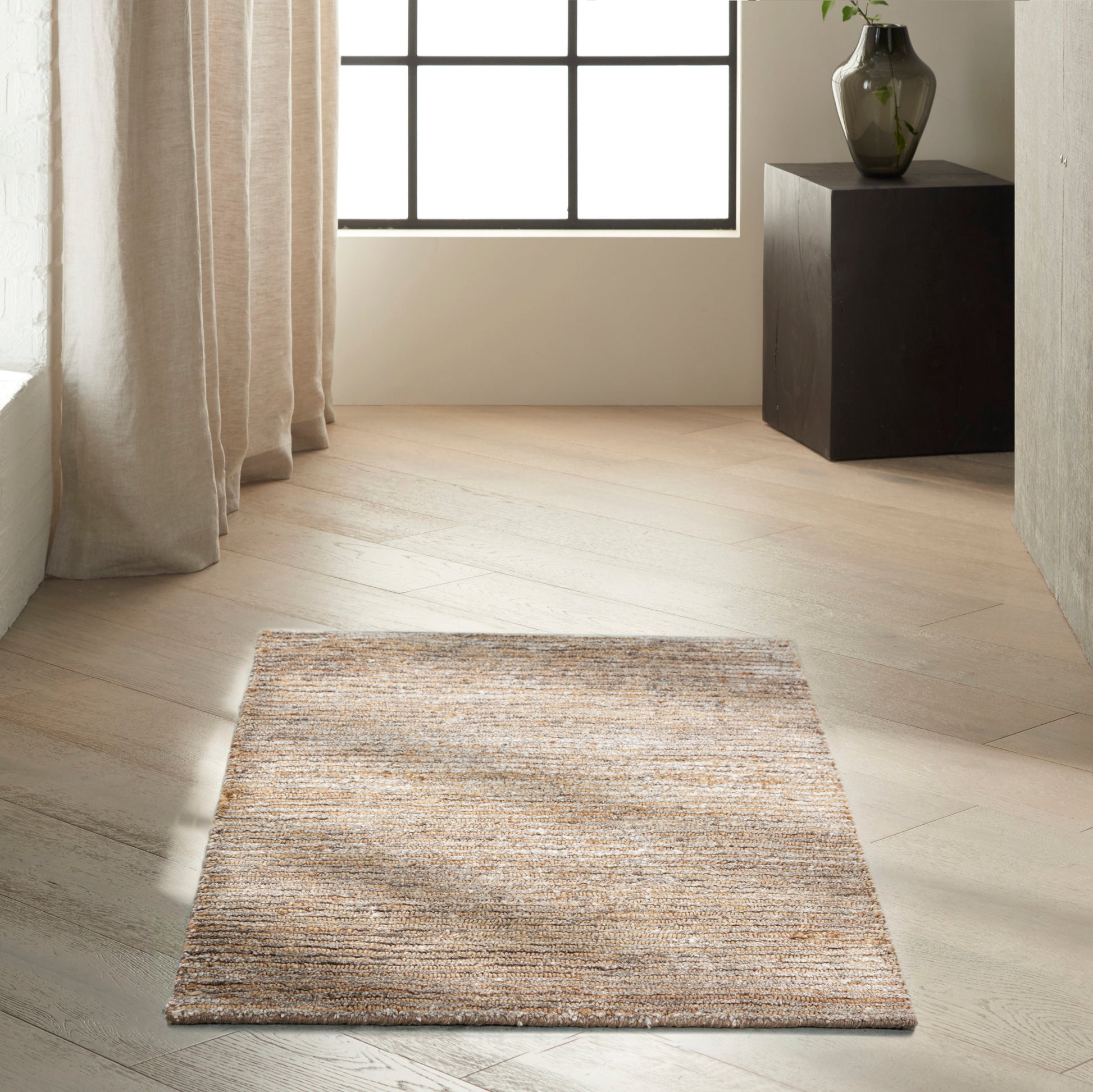 Beige textured rectangular rug on light wood floor in a bright minimalist room with sheer curtains and a dark pedestal with vase.