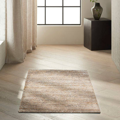 Beige textured rectangular rug on light wood floor in a bright minimalist room with sheer curtains and a dark pedestal with vase.