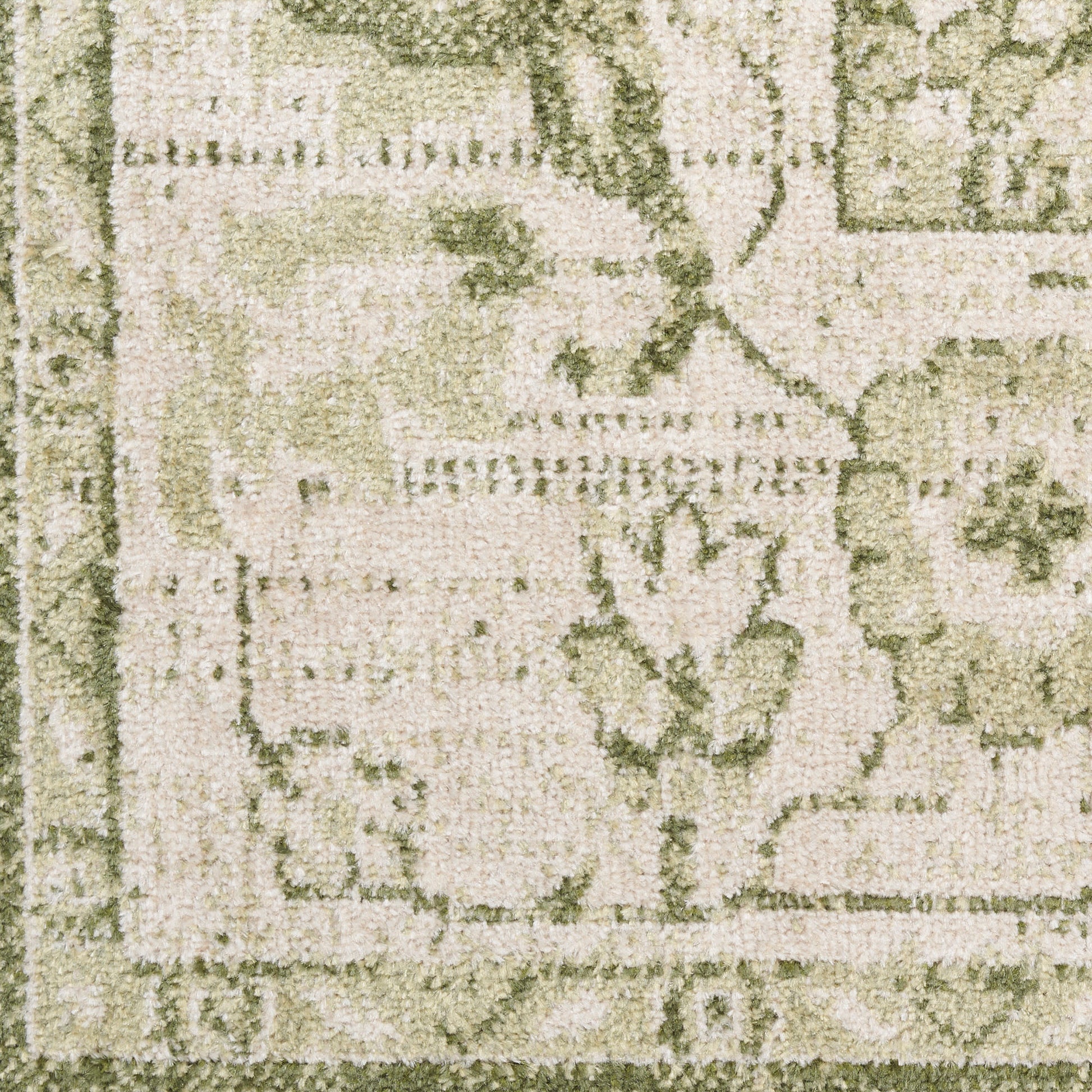Close-up of a beige-green textured rug with floral motifs and a decorative border.