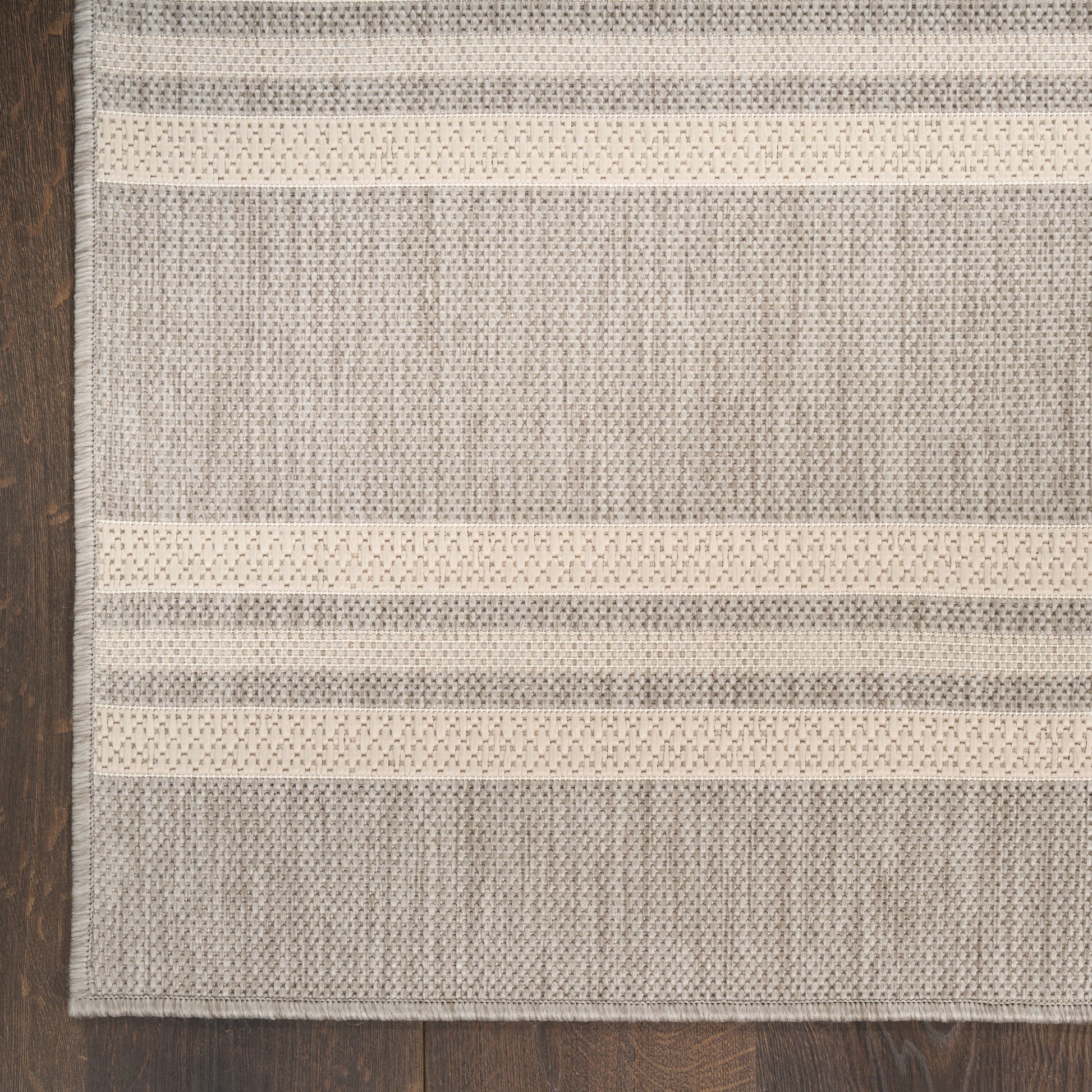 Neutral gray and cream striped woven rectangular rug on dark wood floor.