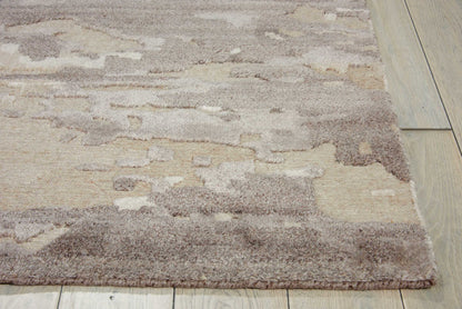 Soft shag area rug in beige and taupe with abstract pattern on light wood floor.