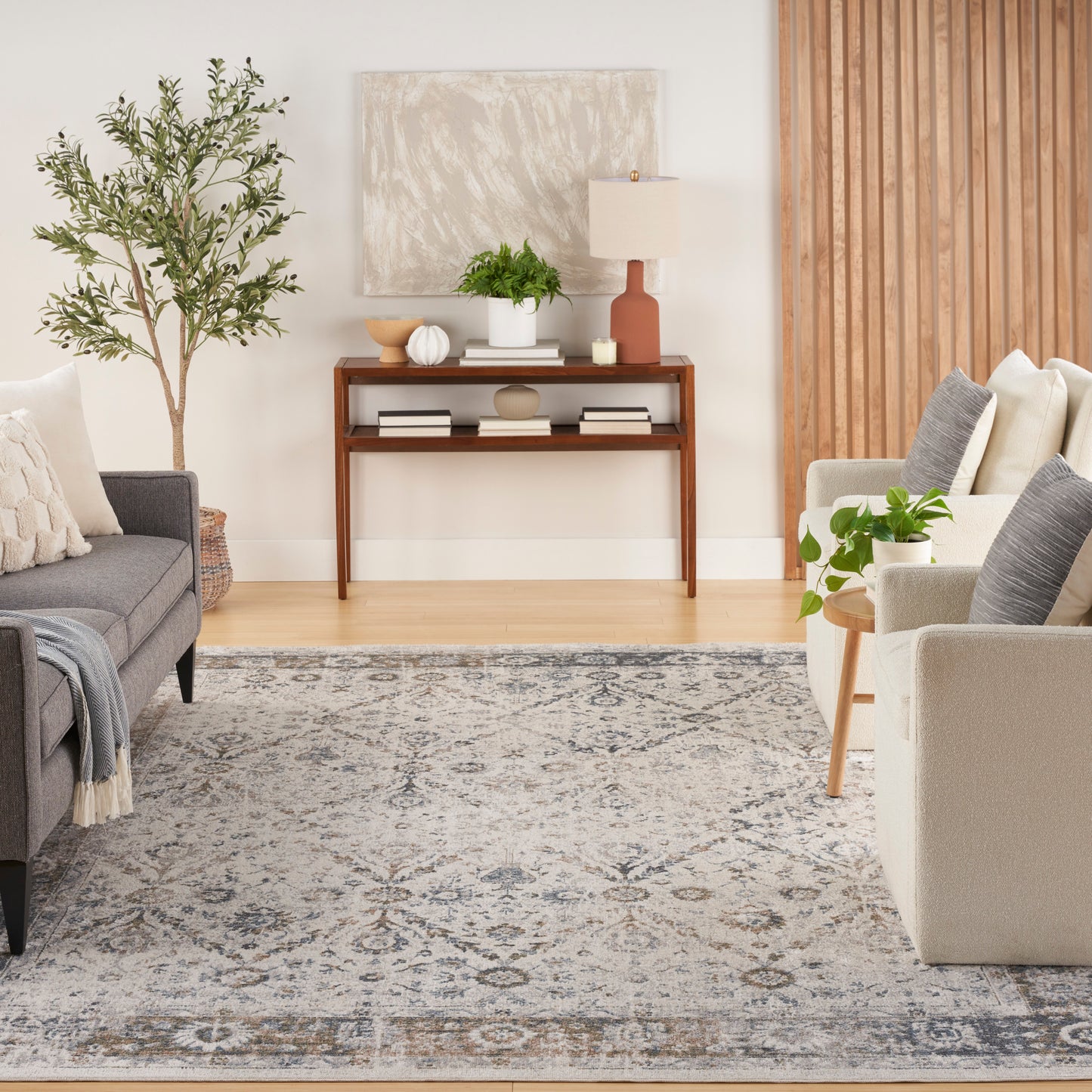 Dark wood console with ceramic lamp and plant, flanked by gray and beige sofas on a blue-gray patterned rug.
