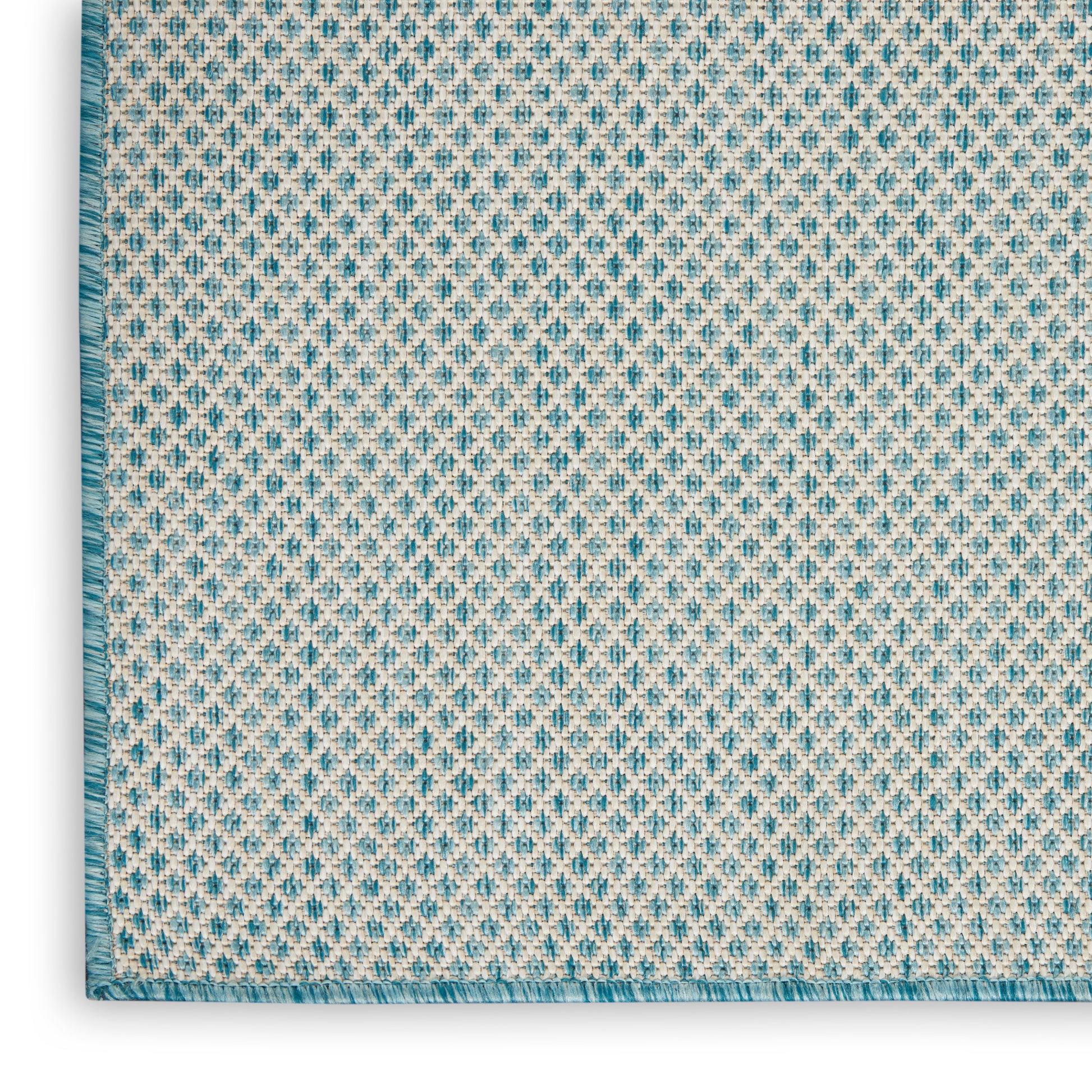 Woven rug close-up: beige base with turquoise geometric pattern, teal border and fringe.