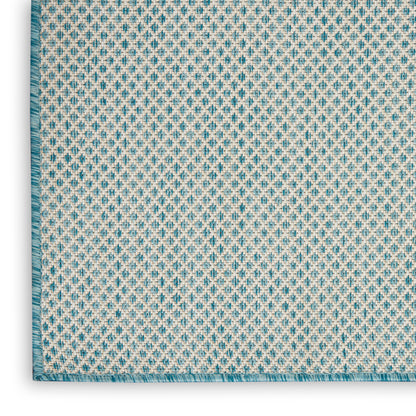 Woven rug close-up: beige base with turquoise geometric pattern, teal border and fringe.