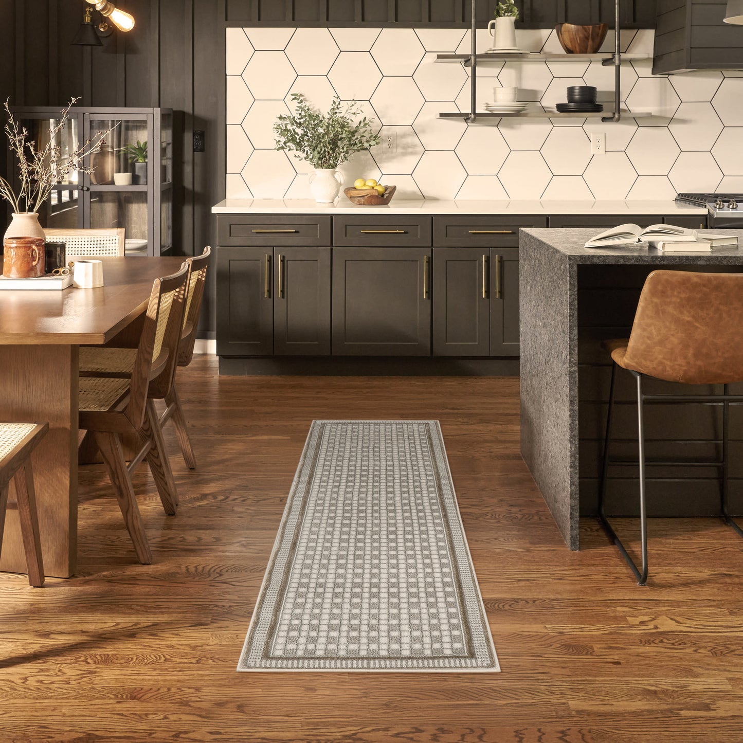 Long light gray geometric lattice rug runner on wood floor in a modern dark kitchen with hex tile backsplash and island seating.