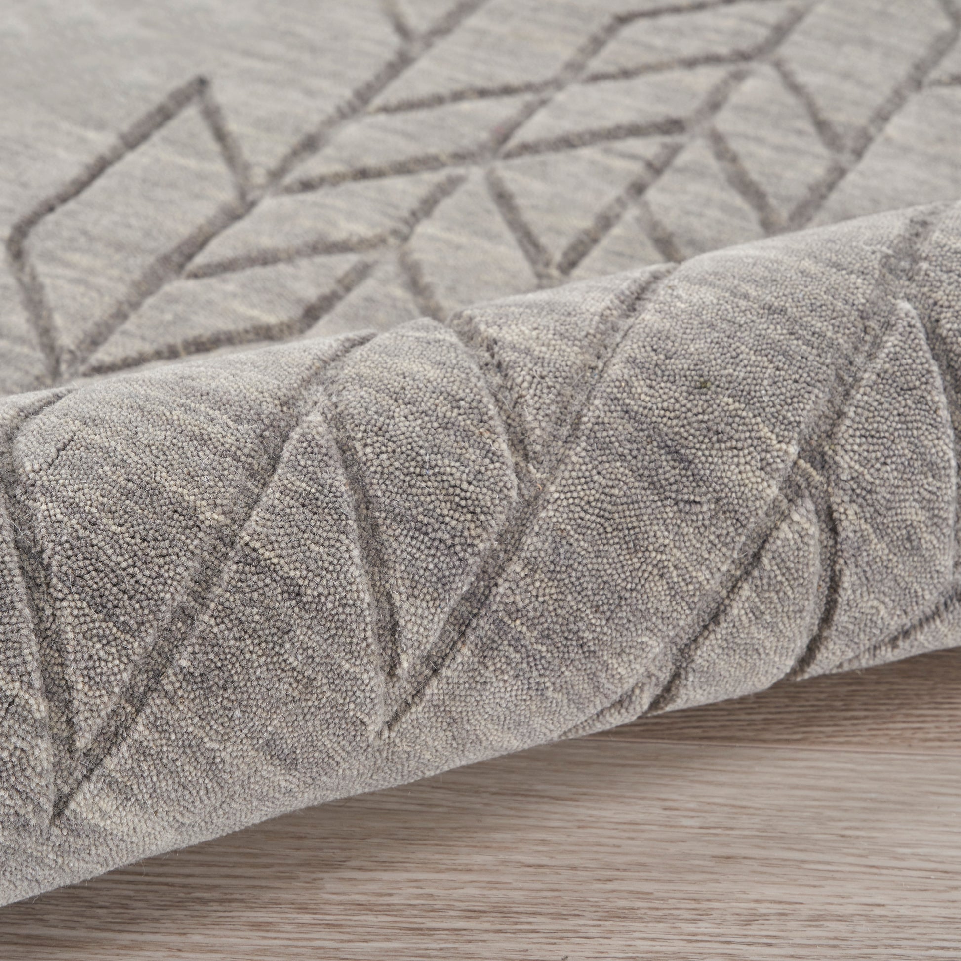 Gray rug with geometric diamond pattern, soft textured pile, folded edge on light wood floor.