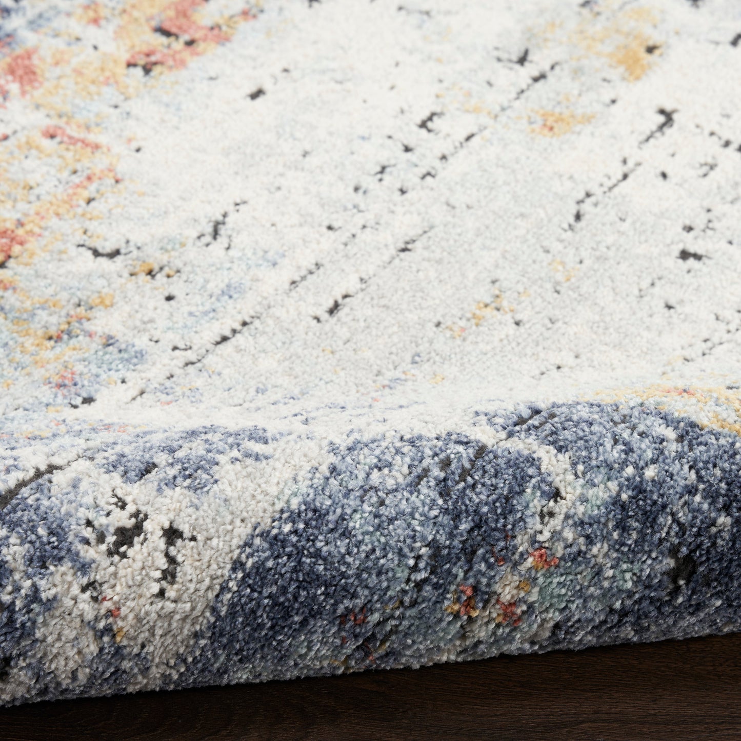 Close-up of a soft pile rug in cream and blue-gray with orange accents; rolled edge reveals an abstract pattern, ideal as an area rug.