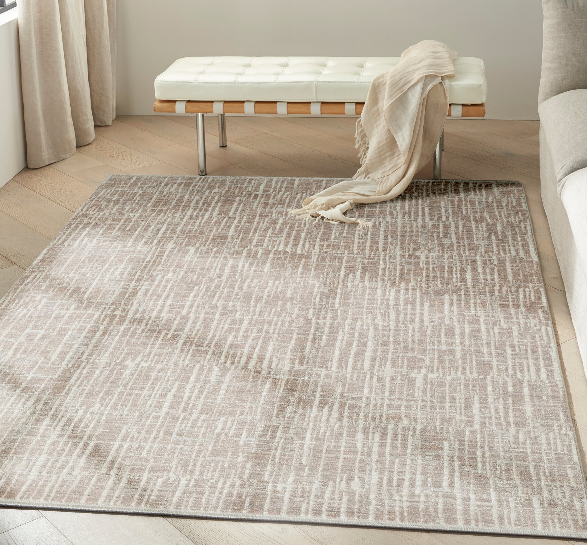 Neutral taupe and cream rug with a linear pattern on light wood floor beside a white tufted bench and beige throw.