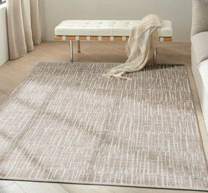 Neutral taupe and cream rug with a linear pattern on light wood floor beside a white tufted bench and beige throw.