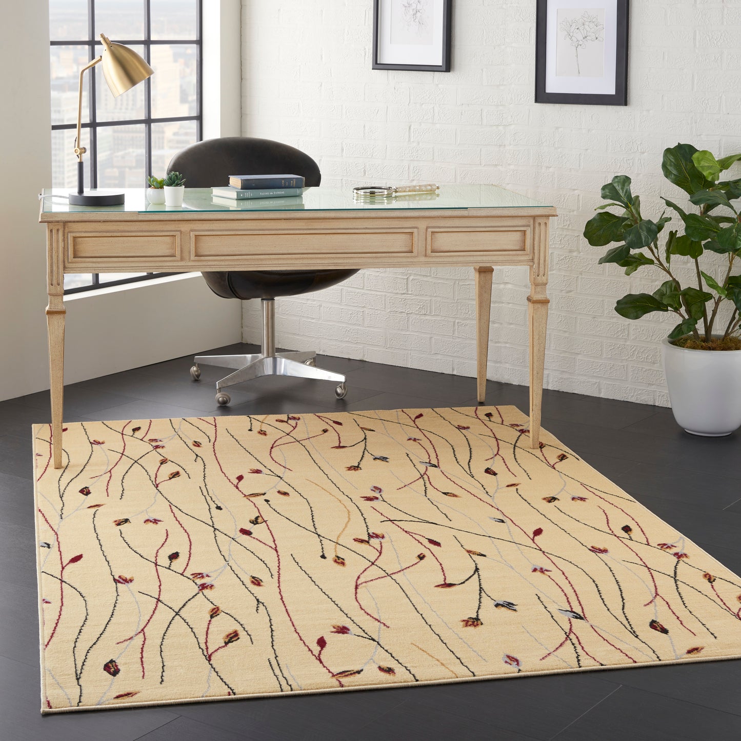 Beige wooden desk with glass top & drawers, black swivel chair, cream rug with abstract vine pattern, potted plant & gold lamp.