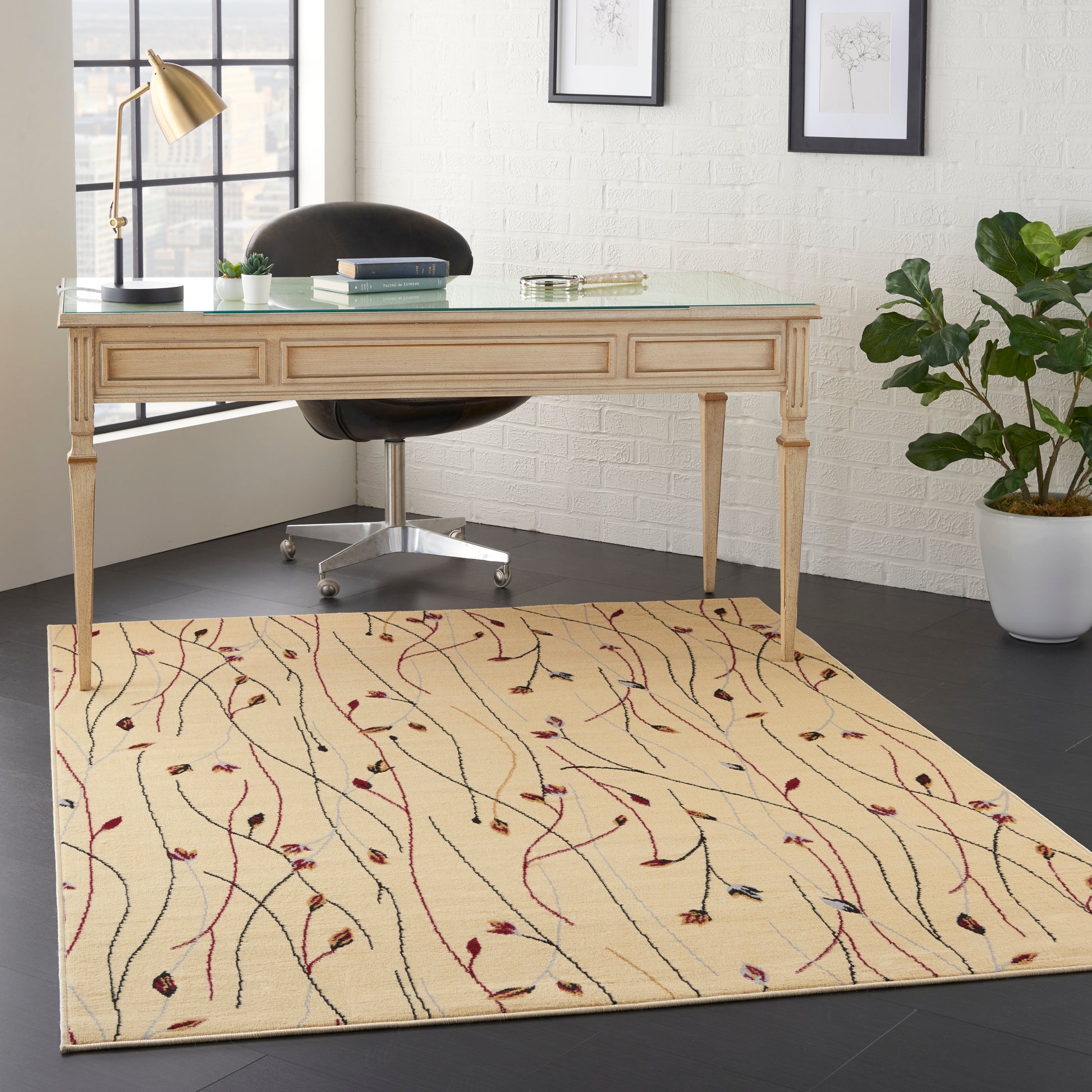 Beige wooden desk with glass top & drawers, black swivel chair, cream rug with abstract vine pattern, potted plant & gold lamp.