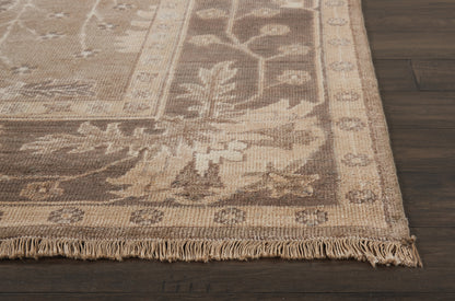 Beige oriental area rug with floral vine pattern and fringed edge on dark wooden floor.