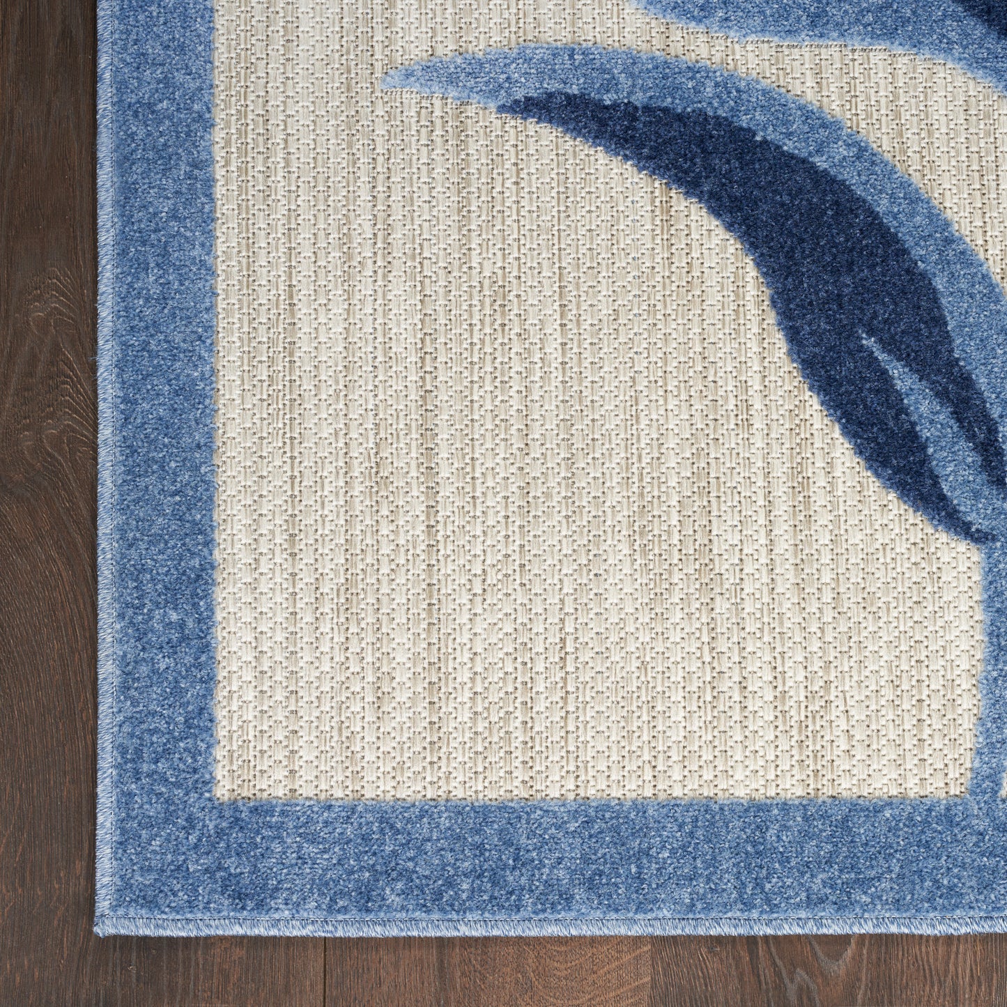 Beige woven area rug with blue border and blue abstract arc motif on dark wood floor.
