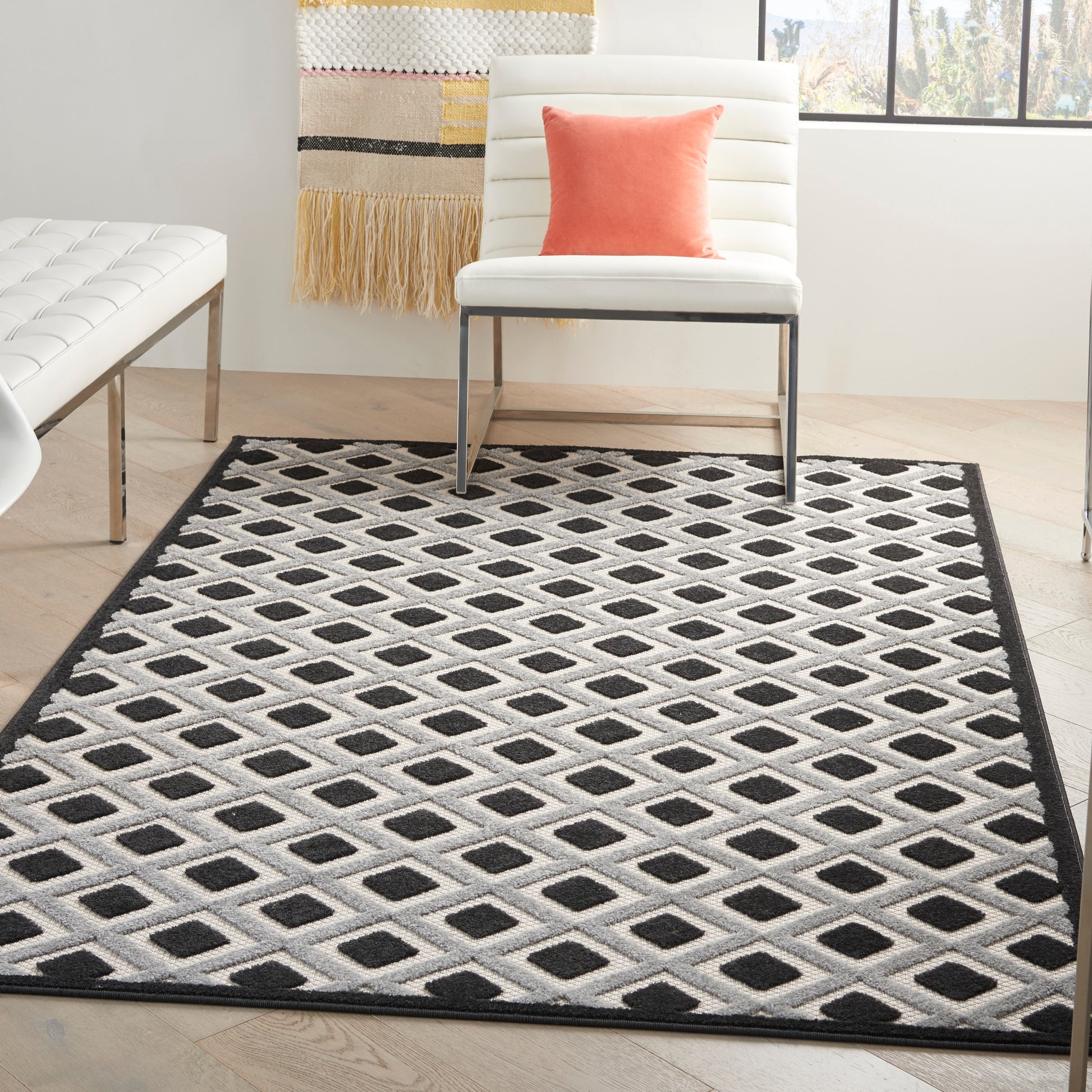 Diamond-patterned black and white rug with a black border; white chair with coral pillow in a modern living room.
