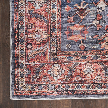 Persian-style wool rug with red and navy field, floral medallions and ornate borders, white fringe along edge on wood floor.